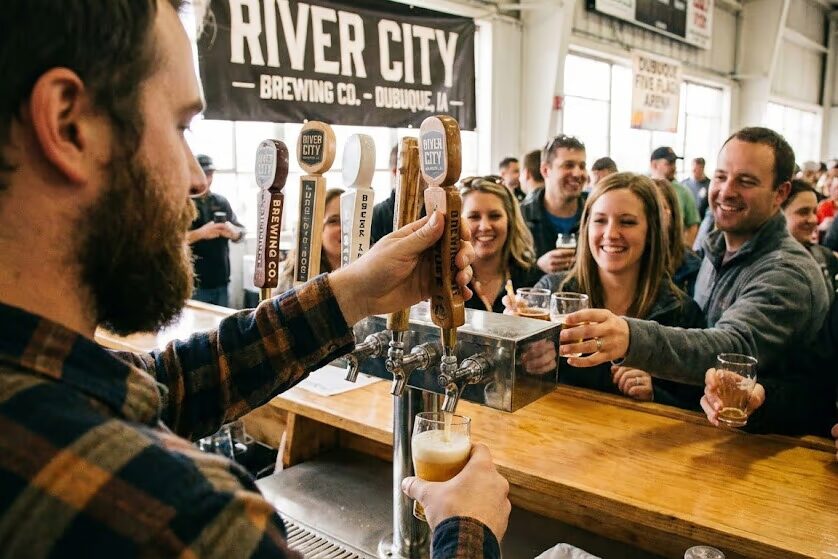 Craft brewery vendor pouring beer samples at Dubuque brewfest with tap handles and attendees at Iowa craft beer event