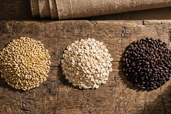 Three piles of Irish dry stout brewing grains — pale malt, flaked barley, and roasted barley — arranged on a rustic wooden surface