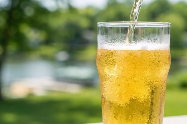 A pale golden American craft lager being poured into a pint glass outdoors on a sunny summer day with condensation on the glass